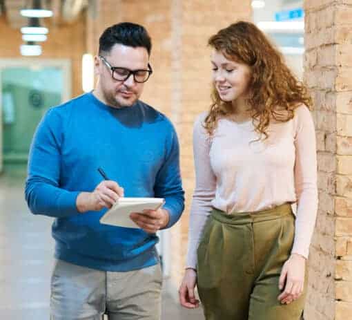 Man glass and woman with green pants go over notes on notepad