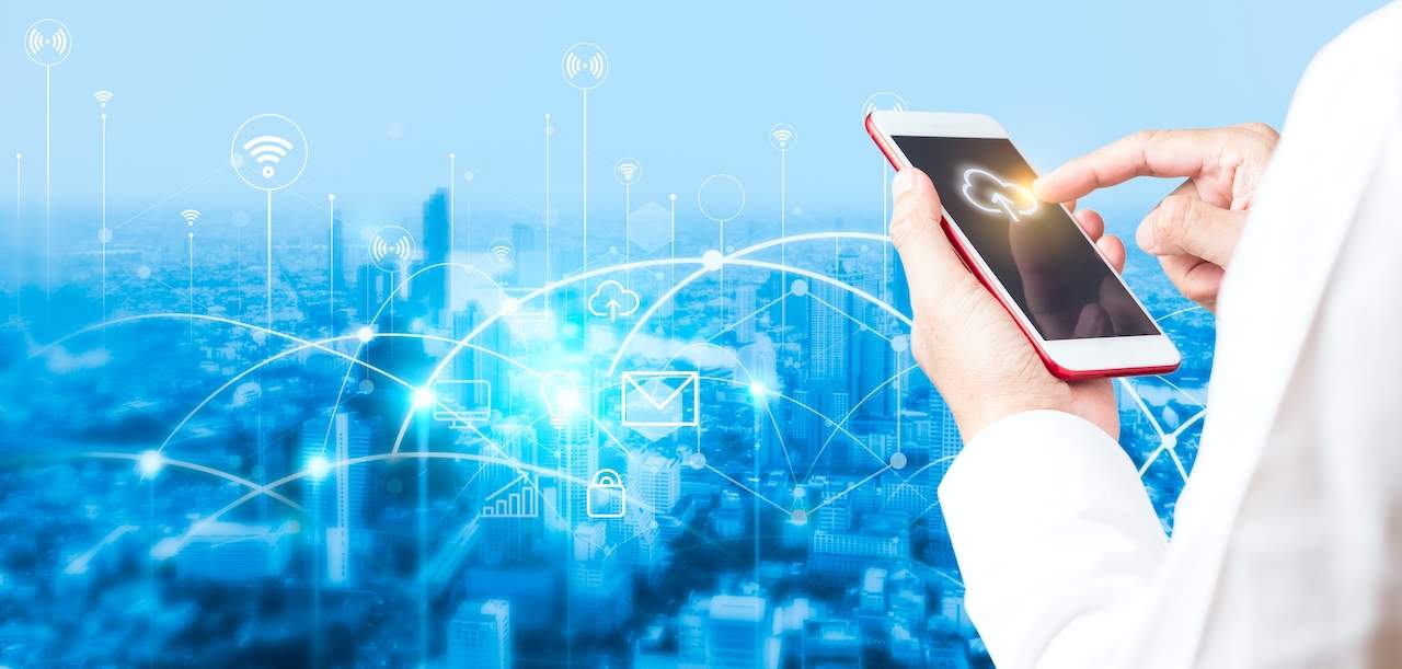 A man in a white coat holding a smart phone in front of a city, showcasing cloud security solutions.
